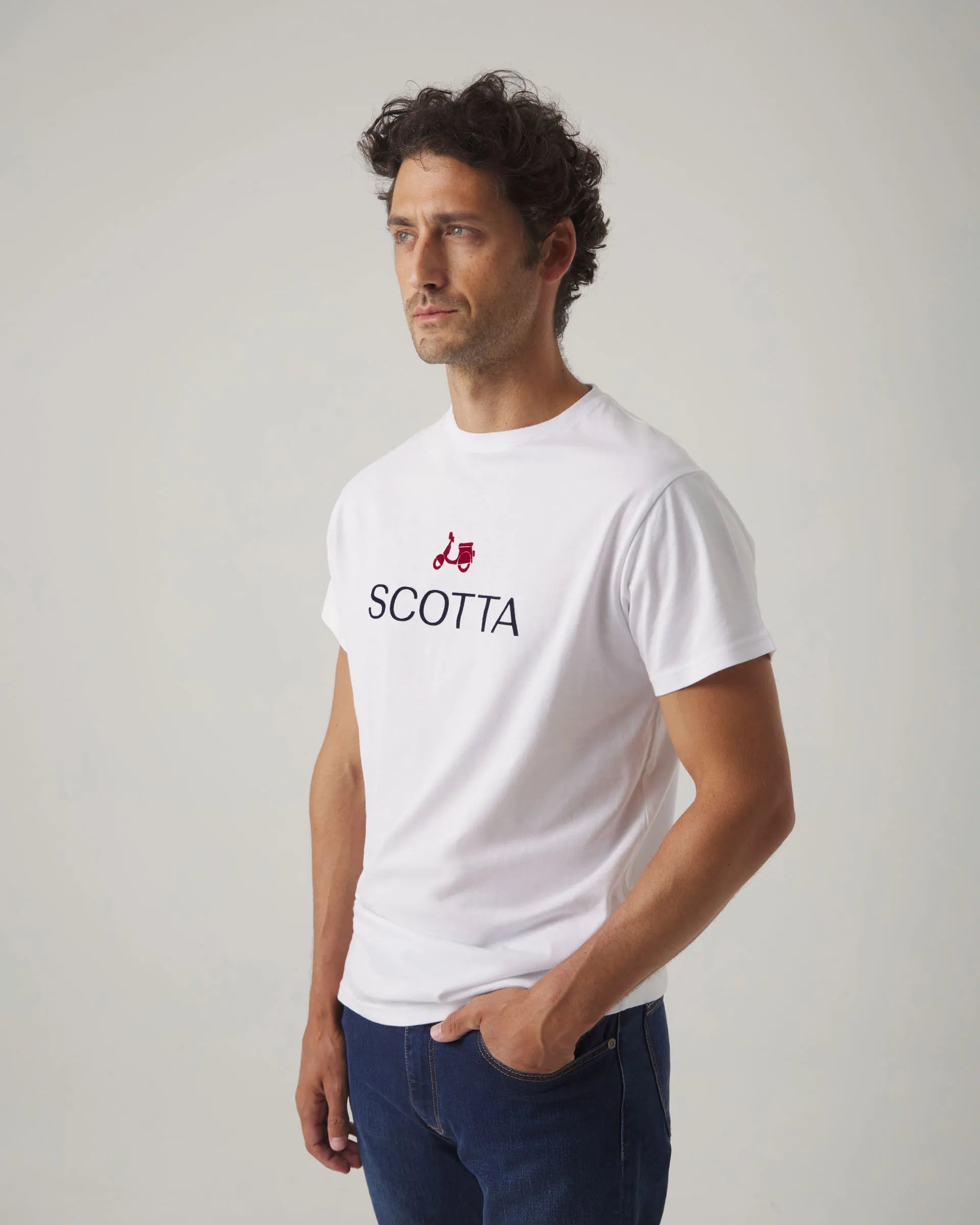 Camiseta blanca con cuello redondo y manga corta, con letras y moto Scotta en el torso.
